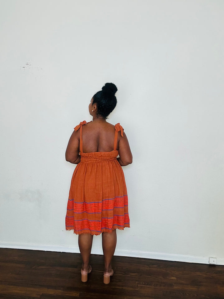Gelila Dress Cinnabar Glow — handmade 100% cotton midi dress with straight neckline, adjustable straps, cinched waist, flowing skirt, and hidden pockets in a deep burnt orange tone.