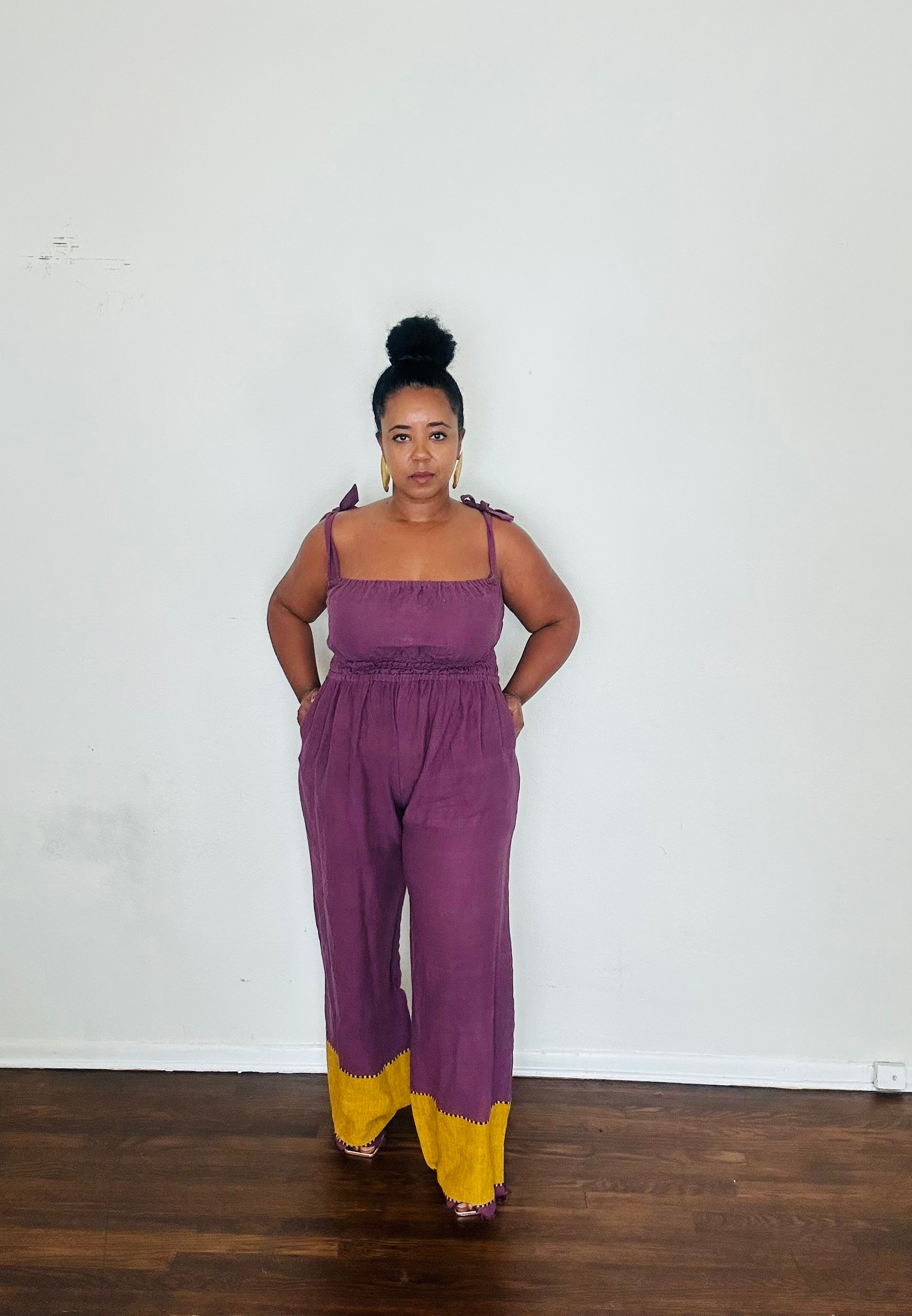 Sebie Jumpsuit in Purple Reign — 100% cotton, handmade in Ethiopia, featuring a regal royal purple tone with a rich golden hem.