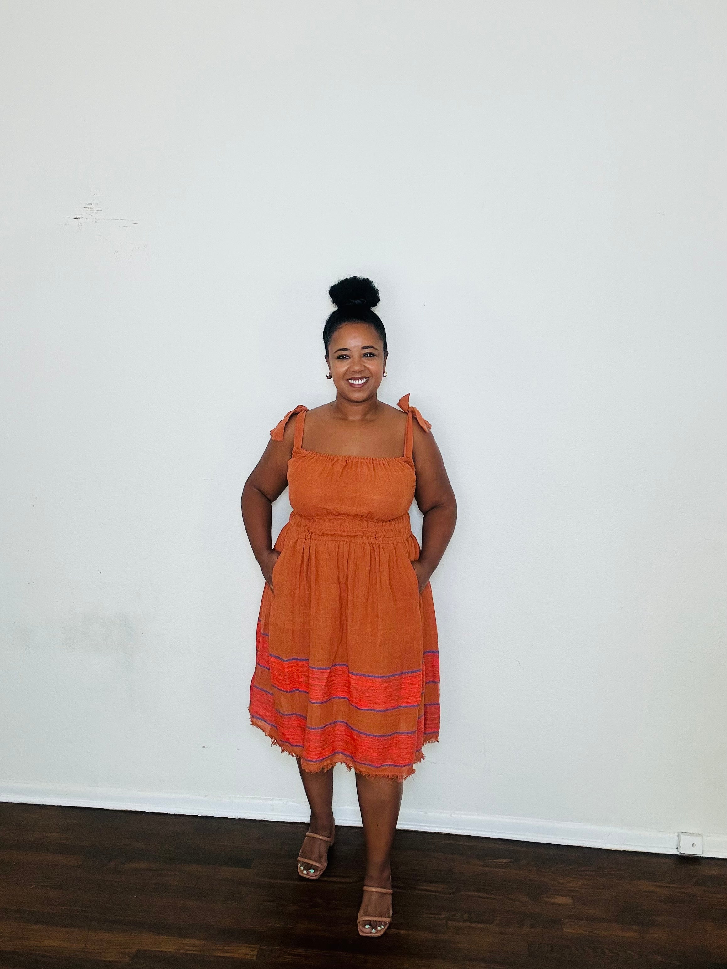 Gelila Dress Cinnabar Glow — handmade 100% cotton midi dress with straight neckline, adjustable straps, cinched waist, flowing skirt, and hidden pockets in a deep burnt orange tone.