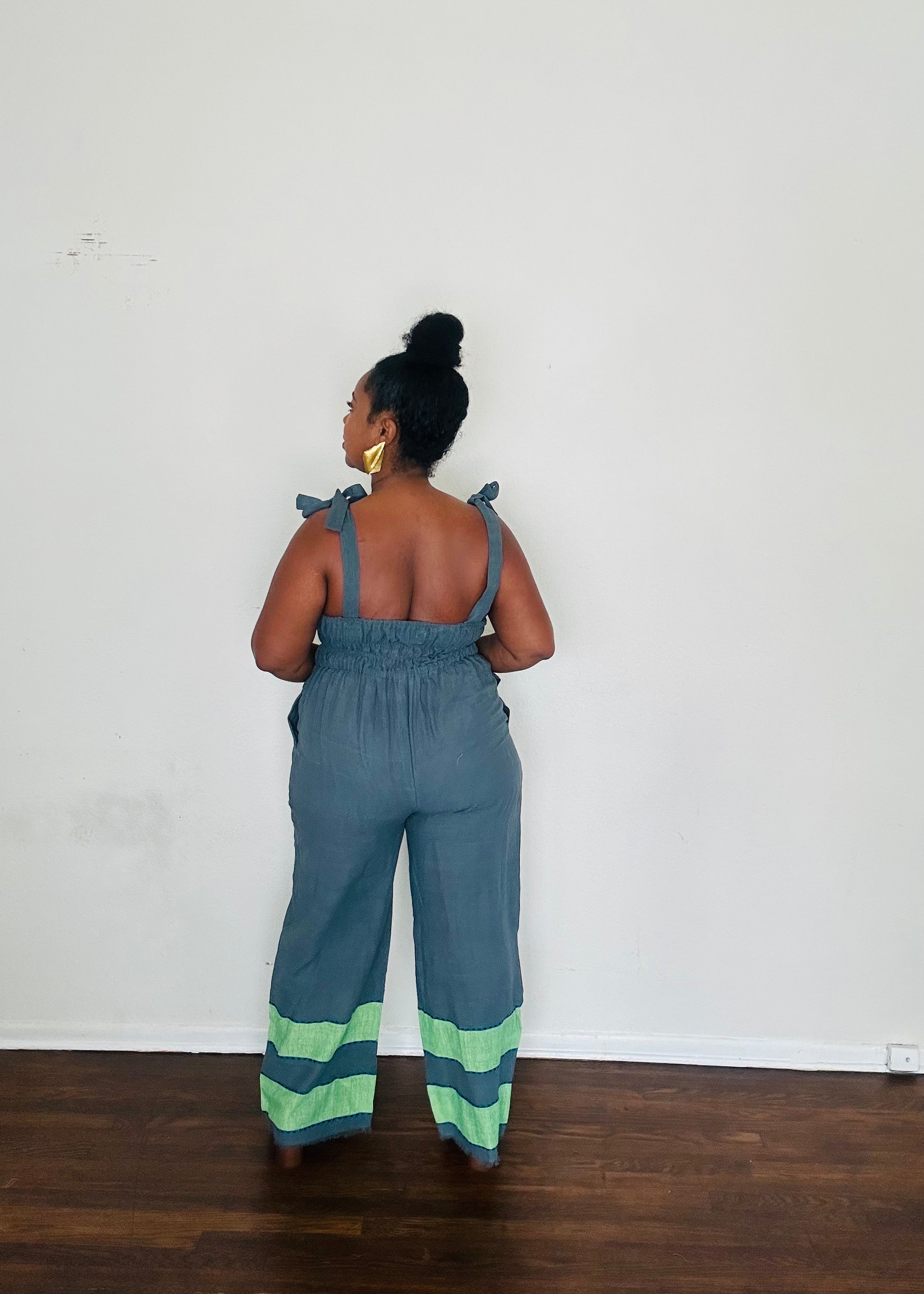 Handmade Blue Slate Sebie Jumpsuit in 100% cotton, featuring a flattering waist, adjustable straps, and deep pockets. Finished with a signature brown hem detailed with lime green accents for a bold, free-spirited LA style