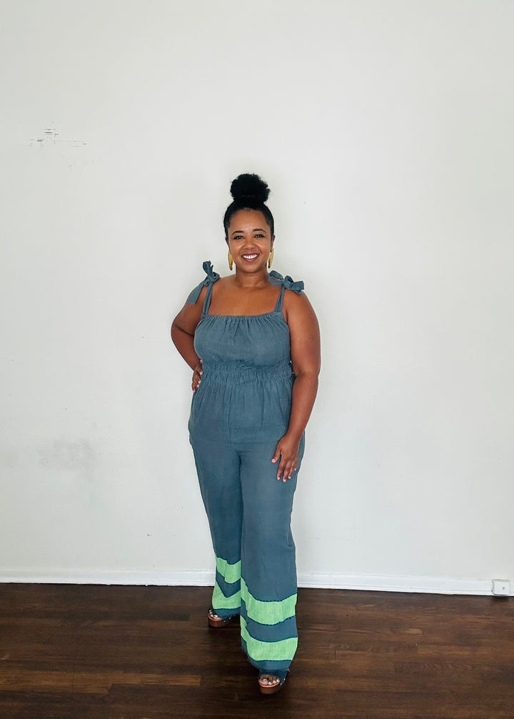Handmade Blue Slate Sebie Jumpsuit in 100% cotton, featuring a flattering waist, adjustable straps, and deep pockets. Finished with a signature brown hem detailed with lime green accents for a bold, free-spirited LA style