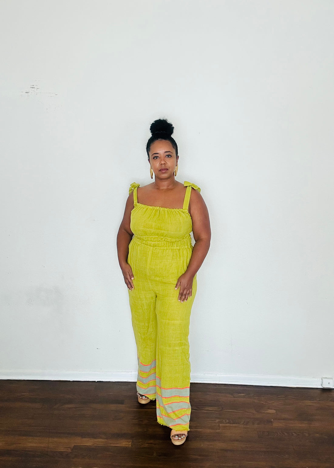 Handmade Chartreuse Sebie Jumpsuit in 100% cotton, featuring a flattering waist, adjustable straps, and deep pockets. Finished with a signature brown hem detailed with lime green accents for a bold, free-spirited LA style