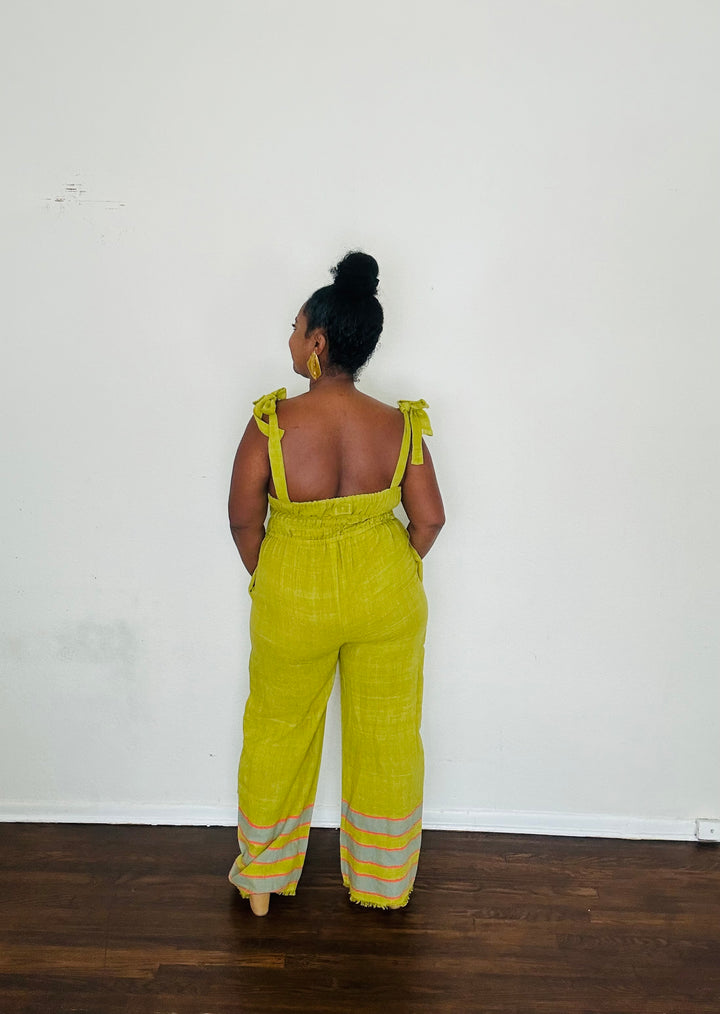 Handmade Chartreuse Sebie Jumpsuit in 100% cotton, featuring a flattering waist, adjustable straps, and deep pockets. Finished with a signature brown hem detailed with lime green accents for a bold, free-spirited LA style