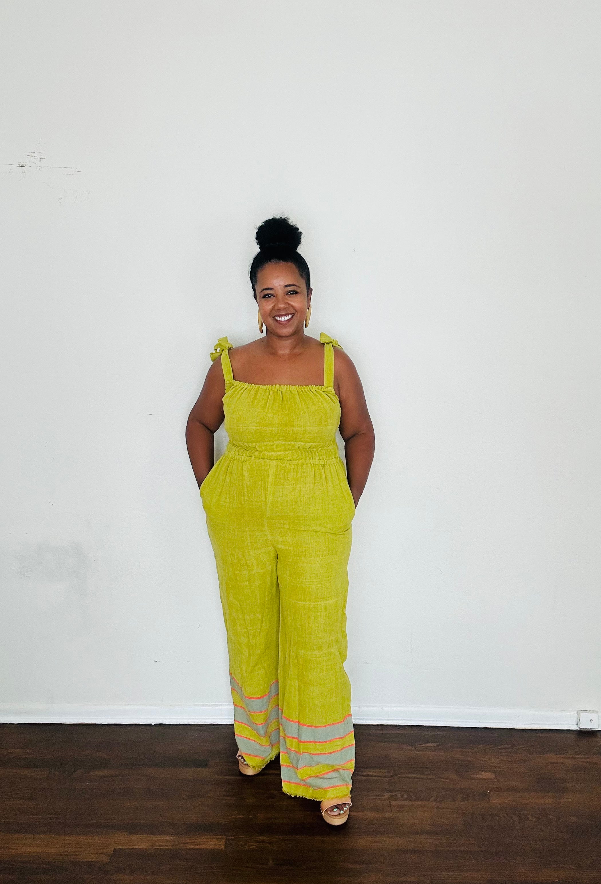 Handmade Chartreuse Sebie Jumpsuit in 100% cotton, featuring a flattering waist, adjustable straps, and deep pockets. Finished with a signature brown hem detailed with lime green accents for a bold, free-spirited LA style