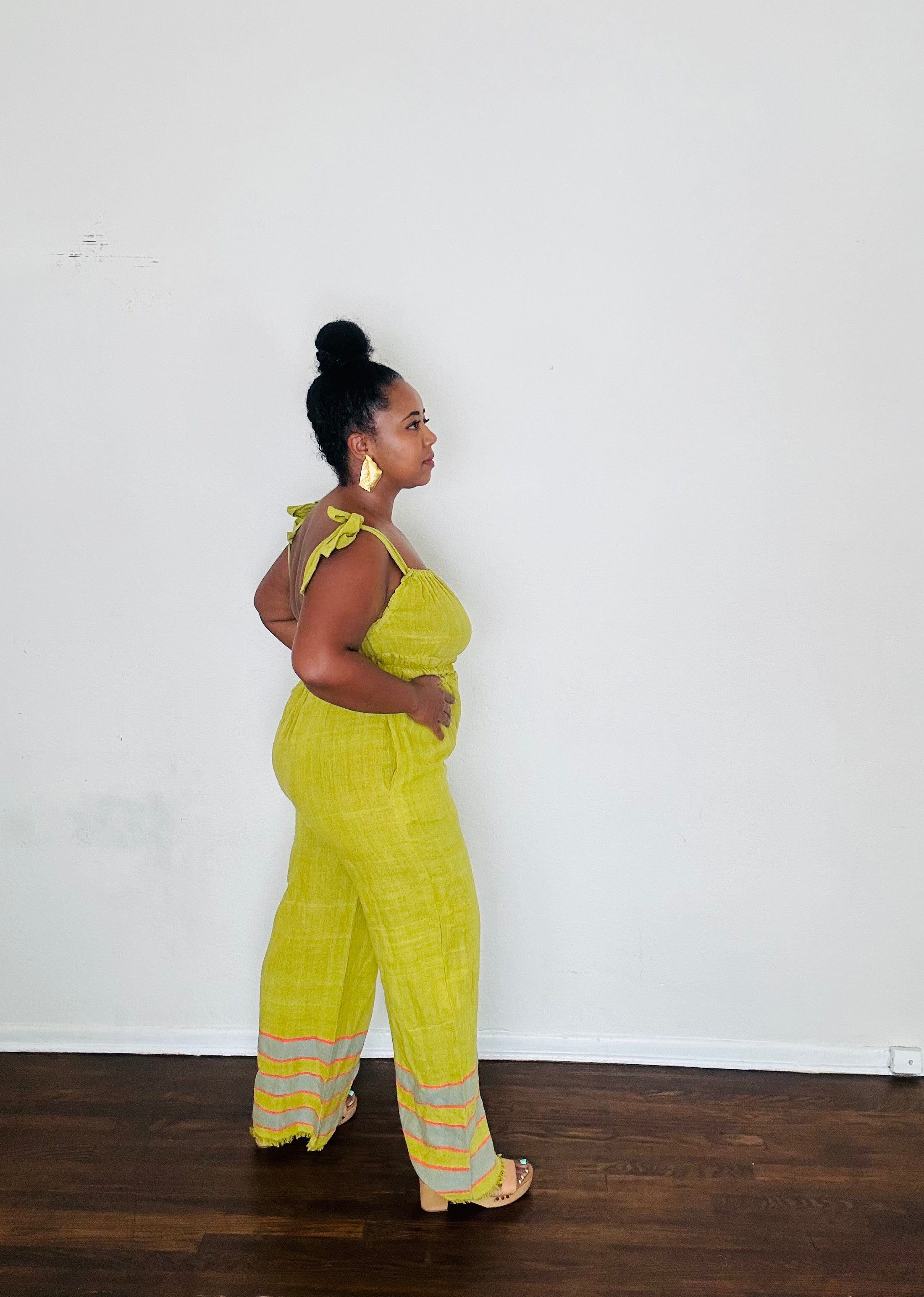 Handmade Chartreuse Sebie Jumpsuit in 100% cotton, featuring a flattering waist, adjustable straps, and deep pockets. Finished with a signature brown hem detailed with lime green accents for a bold, free-spirited LA style