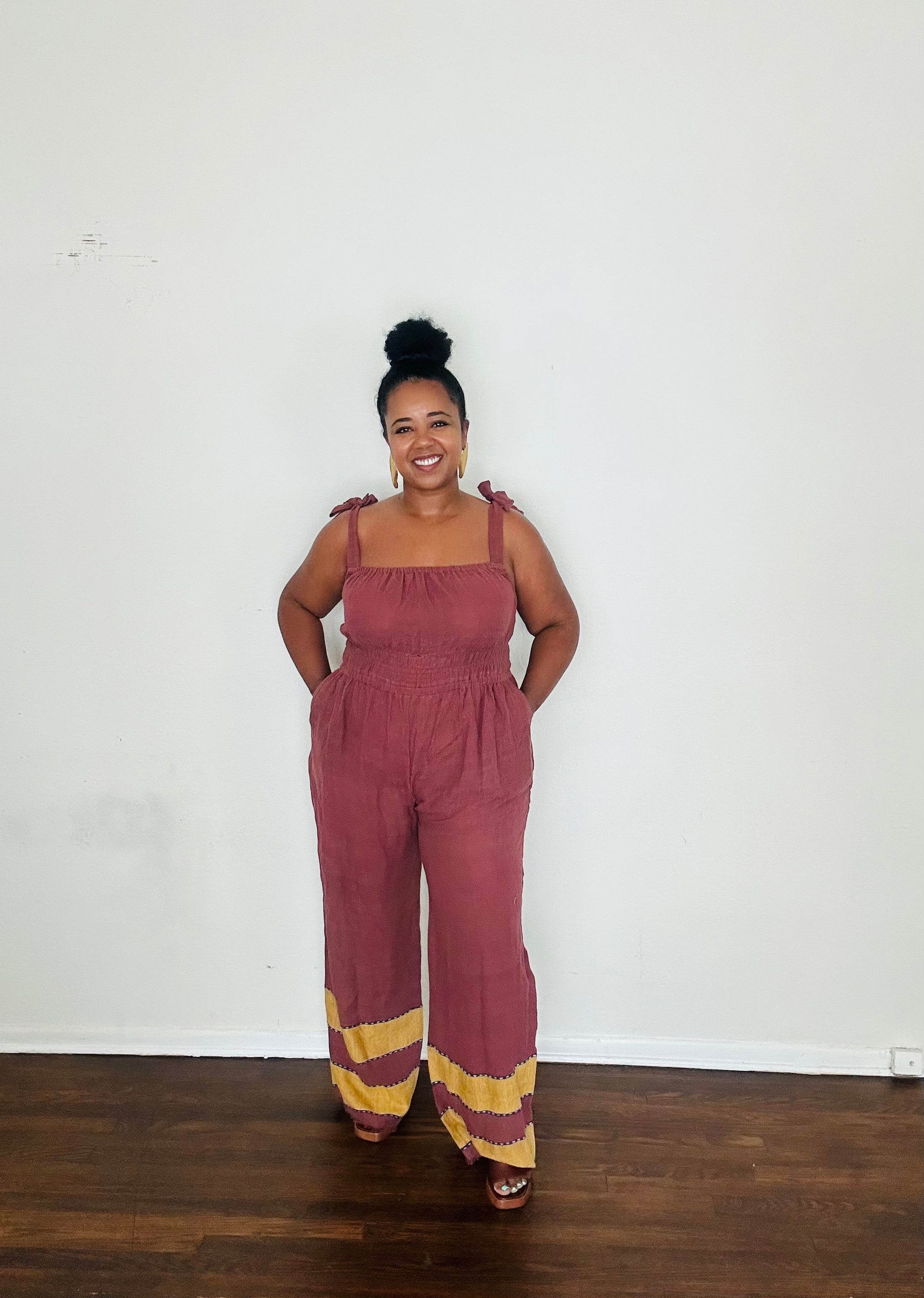 Handmade Plum Eclipse  Sebie Jumpsuit in 100% cotton, featuring a flattering waist, adjustable straps, and deep pockets. Finished with a signature brown hem detailed with lime green accents for a bold, free-spirited LA style