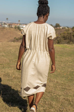 1) The Aki Dress is a simple natural ecru dress with a bold pop of color along the skirt. The big diamond pattern gives the dress a simple yet impactful elegance.   2) The Aki Dress features a waist-tie that cinches the relaxed silhouette and gives the waist a more fitted line.  3) Made in Ethiopia by Menby Design. Menby seeks to empower Ethiopian woman with economic independence through skills training and employment.